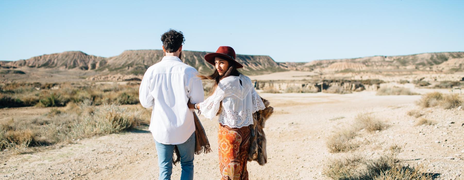 a man and woman walking on a dirt road in the desert